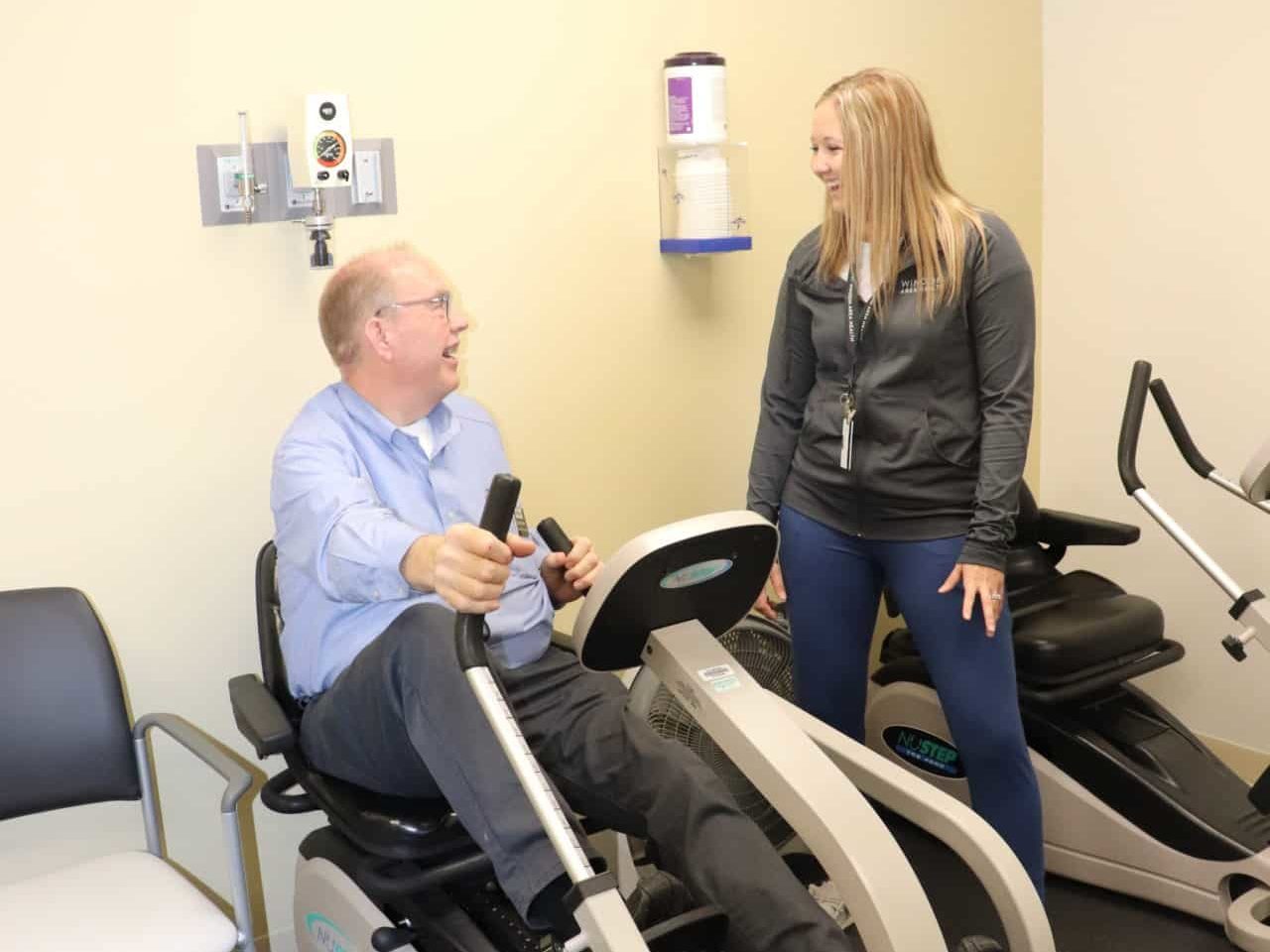 Pictured: Lacy Krueger working with Dan on a NuStep machine during a workout in the Cardiac Rehabilitation room.